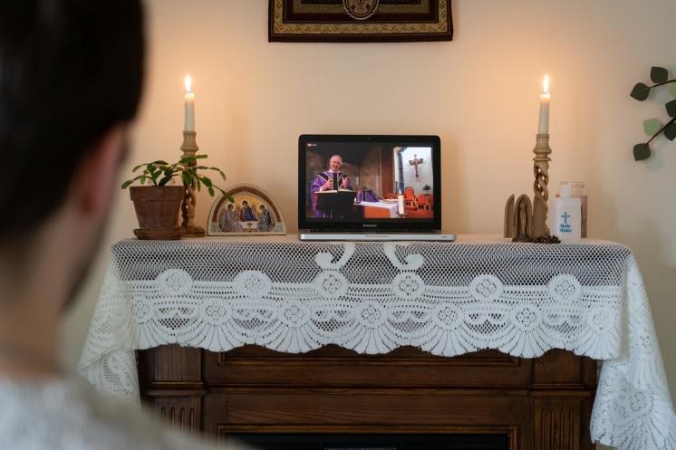 Mass livestream on a laptop in someone's home altar with candles