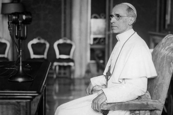 Pope Pius XII sits in front of a microphone.